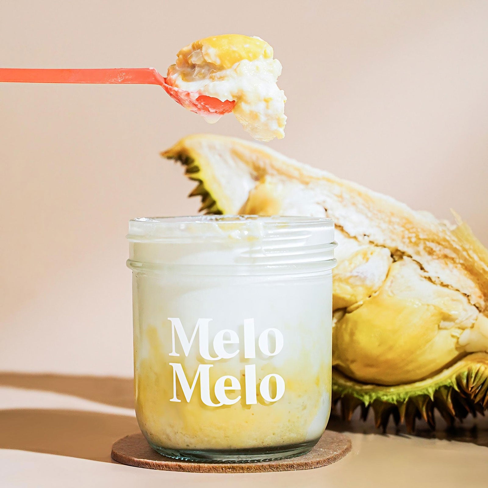 durian coconut jelly in glass jar, creamy coconut jelly with musang king durian chunks, spoon lifting rich jelly, dripping texture, fresh durian fruit in background, clean beige background, soft natural light, premium dessert photography