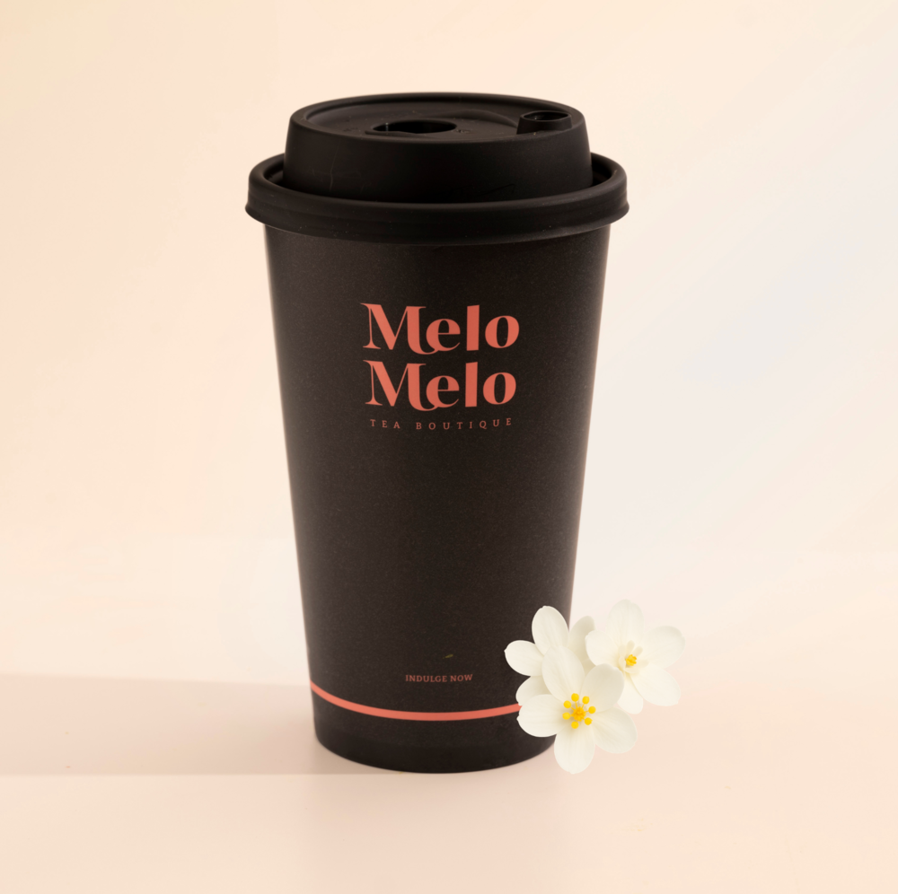 Minimalist product shot of a premium Jasmine tea boutique branded takeaway cup alongside loose leaf tea and dried Jasmine flowers, highlighting a modern tea brand presentation.