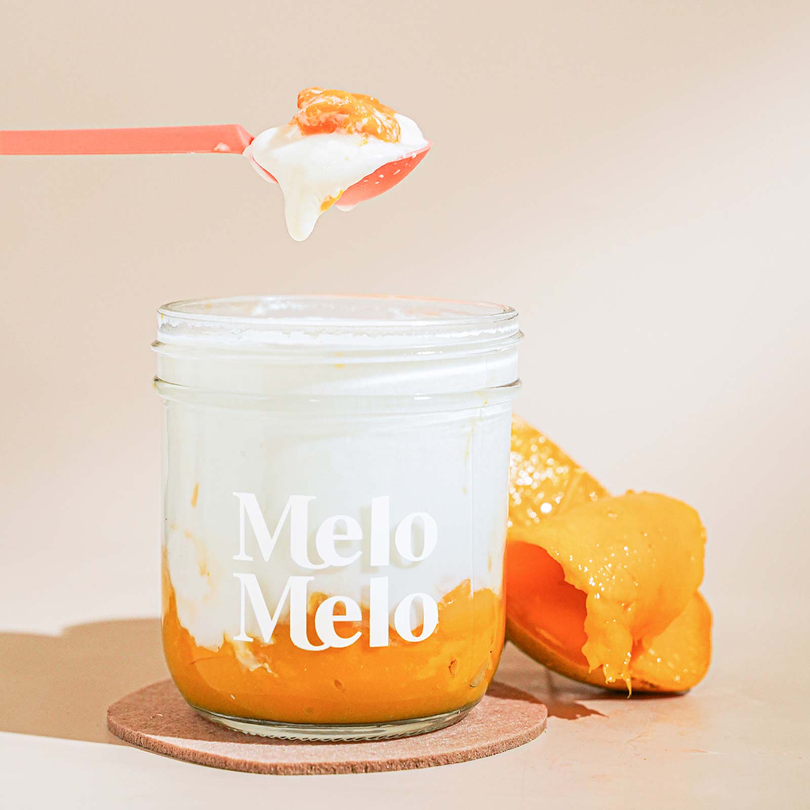 mango coconut jelly dessert in glass jar, silky coconut jelly with mango puree, visible mango chunks, spoon lifting creamy jelly, dripping texture, fresh mango beside, clean beige background, soft natural light, premium food photography