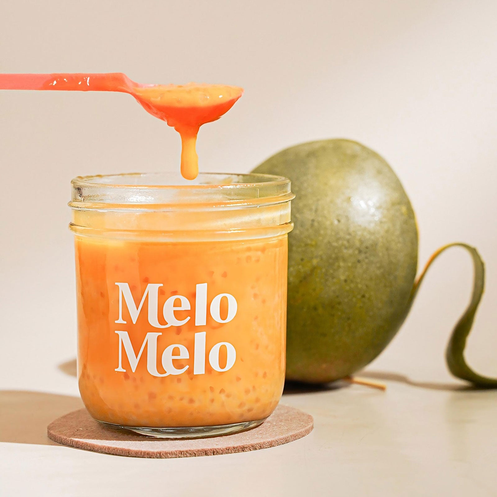 Mango coconut drink with tapioca pearls in a glass jar, featuring a rich orange color, creamy texture, and a spoonful of dripping mango mixture, with a whole mango in the background for a fresh tropical feel.