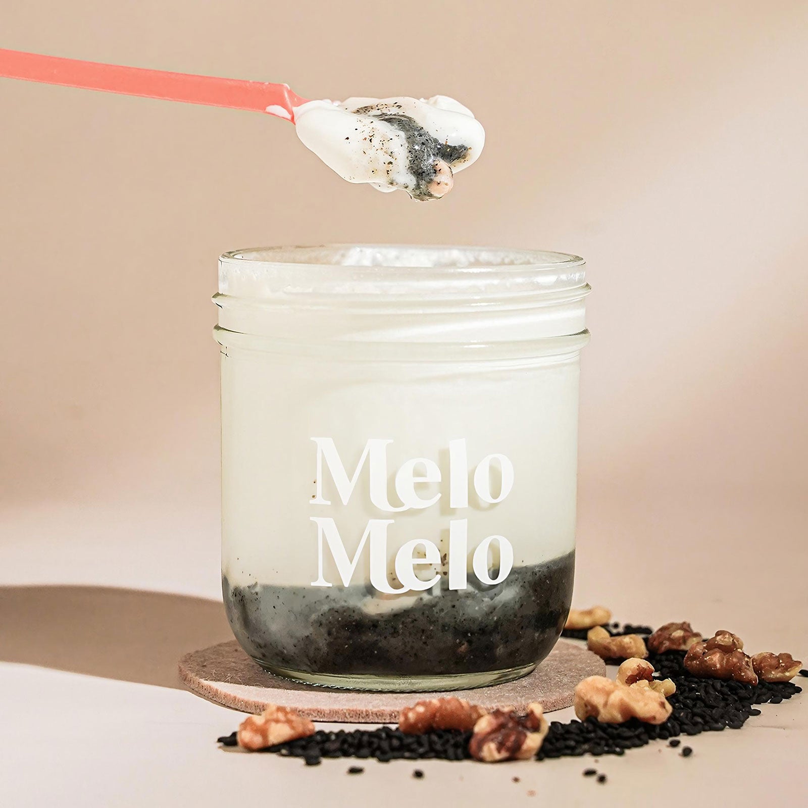 Sesame Walnut coconut jelly in glass jar, creamy coconut layer with  premium sesame paste and high-quality walnuts base, spoon lifting silky jelly, dripping texture, fresh sesame and walnut  beside, clean beige background, soft natural light, premium food photography